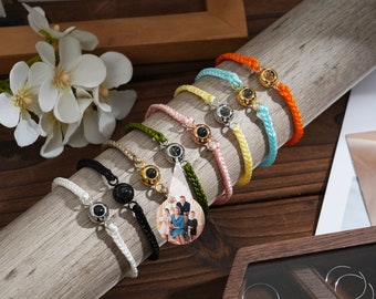 Könnte beinhalten: Ein Set aus bunten Armbändern aus Schnur mit einem kleinen Foto-Anhänger. Der Anhänger zeigt eine vierköpfige Familie. Die Armbänder sind aus verschiedenen Farben von Schnur gefertigt, darunter Weiß, Schwarz, Grün, Gelb, Blau und Orange.