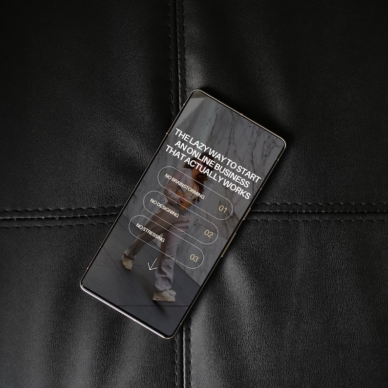 Może przedstawiać: Smartfon wyświetla tekst: "THE LAZY WAY TO START AN ONLINE BUSINESS THAT ACTUALLY WORKS." Ekran pokazuje osobę idącą i wymienia "NO BRAINSTORMING," "NO DESIGNING," i "NO STRESSING." Telefon leży na czarnej sk&oacute;rzanej powierzchni.