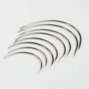 May include: A set of nine silver curved needles, arranged in a fan shape, with the tips pointing to the right.