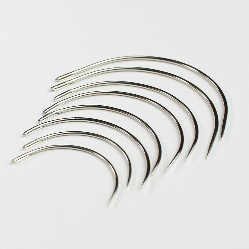 May include: A set of nine silver curved needles, arranged in a fan shape, with the tips pointing to the right.