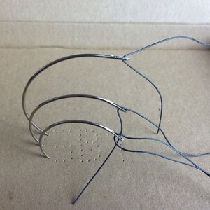May include: Three curved needles of different sizes with black thread looped through the eye of each needle.