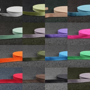 Könnte beinhalten: Sortiment aus 12 Farben Baumwoll-Twillband, jede Farbe wird auf einer separaten Rolle gezeigt. Das Band ist 25 mm breit und hat eine Fischgrätenbindung.