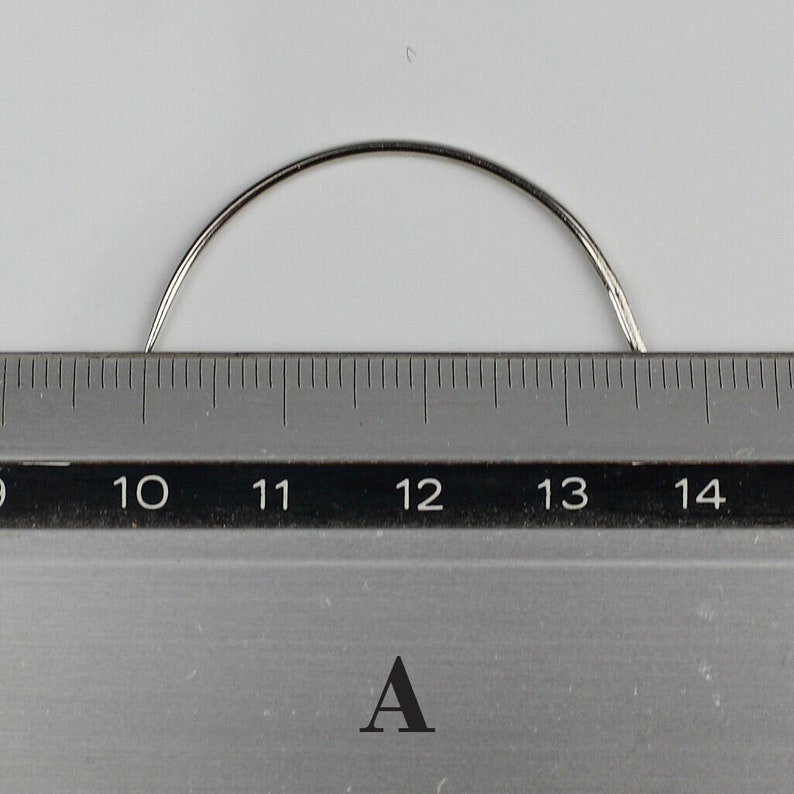 May include: A close-up of a curved, silver needle measuring approximately 12 inches long. The needle is placed on a ruler with markings from 10 to 14 inches.
