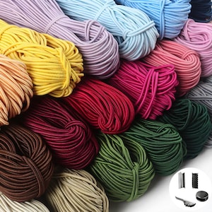 Könnte beinhalten: Eine Sammlung von elastischen Kordelbündeln in verschiedenen Farben, darunter Lavendel, Hellblau, Gelb, Pfirsich, Rosa, Magenta, Rot, Dunkelrot, Braun, Beige, Olivgrün und Dunkelgrün, begleitet von kleinen Kordelverschlüssen aus Metall und Kunststoff.