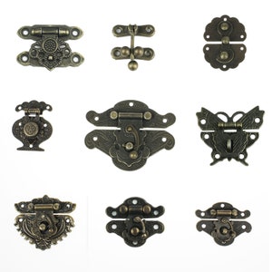 Könnte beinhalten: Neun antike Metallverschlüsse mit filigranen Designs. Die Verschlüsse haben verschiedene Formen, darunter Schmetterlings-, Herz- und Blumenmotive. Sie sind alle in Bronze gehalten.