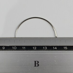 May include: A silver curved needle measuring 14 inches long, placed on a ruler with markings from 9 to 15 inches.