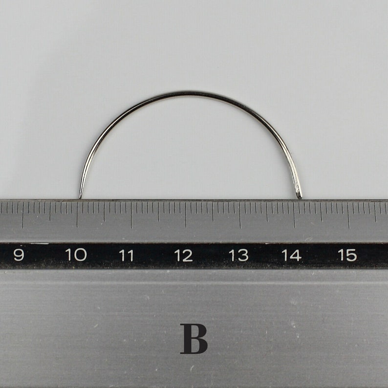 May include: A silver curved needle measuring 14 inches long, placed on a ruler with markings from 9 to 15 inches.
