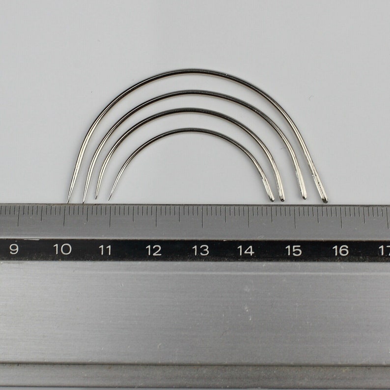 May include: Four silver curved needles of different sizes, measured against a ruler with markings from 9 to 17 inches.