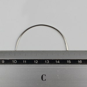 May include: A curved, silver needle measuring 15 inches long. The needle is placed on top of a ruler with markings from 9 to 16.