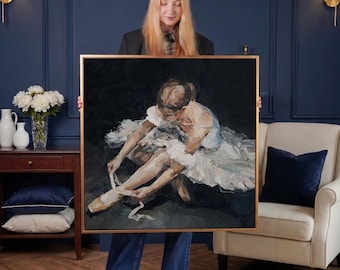 May include: A framed oil painting depicts a ballerina tying her pointe shoe ribbons. The artwork features a palette of white, blue, and neutral tones, with a dark background. The painting is held by a person in a dark blazer and jeans.