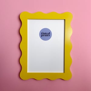 May include: A yellow scalloped picture frame with a white mat and a purple circle with the text "tinted prints" in the center.