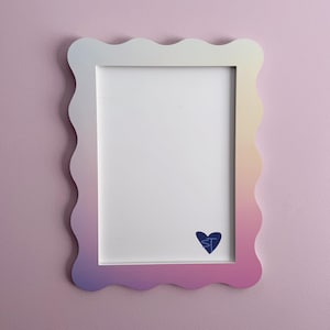 May include: A rectangular picture frame with a wavy, scalloped edge featuring a gradient color transition from yellow at the top right to pink and purple at the bottom left. The white mat board includes a small blue heart icon with the letters ST.