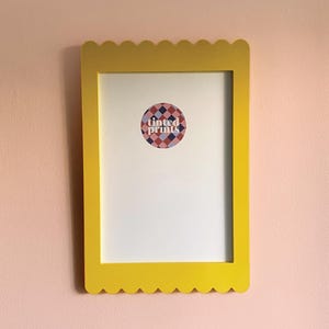 Pode incluir: Uma moldura de imagem amarela com bordas festoneadas, um passe-partout branco e um adesivo que diz "Tinted Prints" em um padrão geométrico colorido.