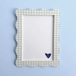 May include: A rectangular picture frame with a scalloped edge and a light gray and white gingham pattern. The frame features a white mat board with a dark blue heart icon in the bottom right corner containing the letters ST in a script font.