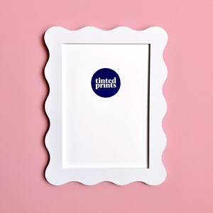 May include: White scalloped picture frame with a white mat and a blue circle with the text "tinted prints" in white.