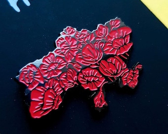 Puede incluir: Un pin de esmalte metálico con la forma del mapa de Ucrania, que presenta un patrón floral de color rojo vibrante en toda su superficie. El diseño consta de múltiples flores rojas estilizadas con contornos negros, creando un aspecto denso.