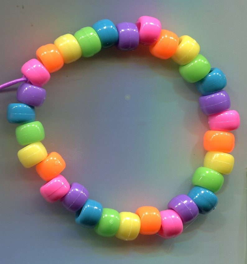 K&ouml;nnte beinhalten: Ein regenbogenfarbenes Perlenarmband mit einer Schnurverschlusses. Die Perlen sind in einem sich wiederholenden Muster aus Rot, Orange, Gelb, Gr&uuml;n, Blau, Indigo und Violett angeordnet.