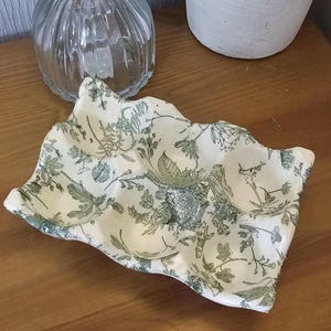 May include: A rectangular ceramic egg tray with a wavy, uneven edge. The surface is off-white and features a detailed, repeating botanical print in a muted sage green colour, depicting various wildflowers, leaves, and stems across the entire piece.