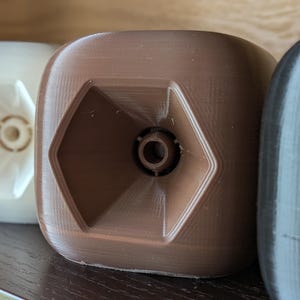 Puede incluir: Primer plano de cuatro objetos cuadrados en fila. Los objetos son de color blanco, marrón y negro. Cada uno tiene un diseño hexagonal en el centro. Los objetos parecen estar impresos en 3D.