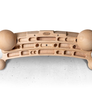 Op de afbeelding: Een houten fingerboard met drie rijen handvatten en twee houten ballen aan de uiteinden. Het fingerboard is gebogen en heeft bovenaan het logo "Hold Fast".