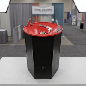 May include: A black hexagonal coin funnel donation stand with a bright red circular top basin. Silver coins are shown spiraling down the red funnel toward the center hole. The base features a small silver key lock mechanism on the front panel.