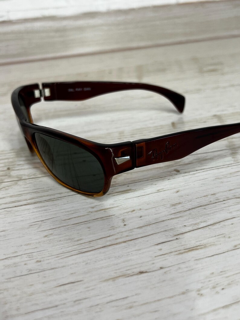 May include: Brown and black sunglasses with a tortoiseshell pattern. The sunglasses have dark lenses and the Ray-Ban logo on the right arm. The frames are a dark brown color.