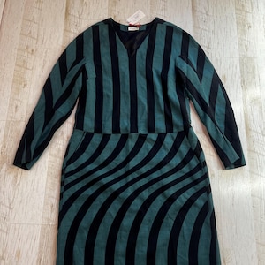 May include: A long-sleeved dress featuring a teal and black colour scheme. The bodice displays vertical stripes, while the skirt section showcases a curved, swirling stripe pattern. The garment has a V-neckline and includes a small white retail tag.