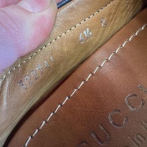 May include: Close-up of the interior of a brown leather shoe. The shoe has a stitched design and the size is marked as 6 1/2. The brand name "GUCCI" is embossed on the leather.