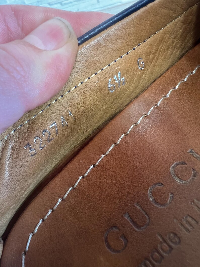 May include: Close-up of the interior of a brown leather shoe. The shoe has a stitched design and the size is marked as 6 1/2. The brand name "GUCCI" is embossed on the leather.