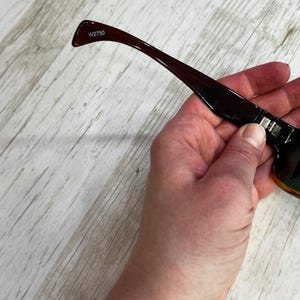 May include: Dark brown sunglasses with a rectangular frame and a gradient lens. The temple arm is a darker shade of brown with the text "W2750" printed on the arm.
