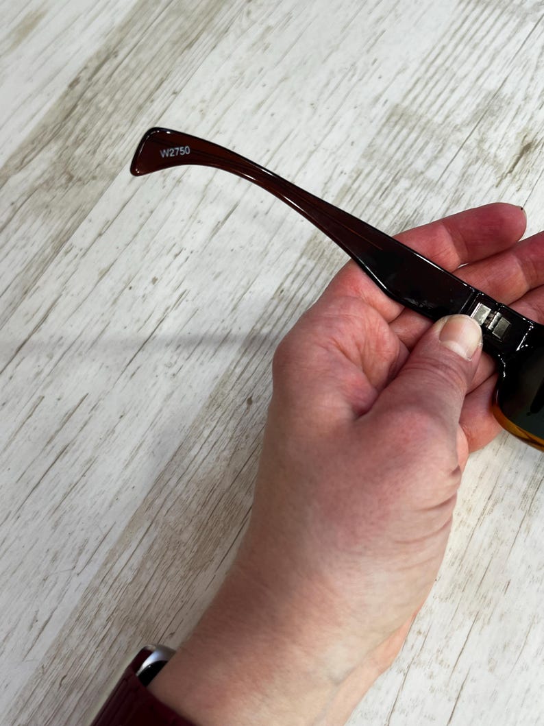 May include: Dark brown sunglasses with a rectangular frame and a gradient lens. The temple arm is a darker shade of brown with the text "W2750" printed on the arm.