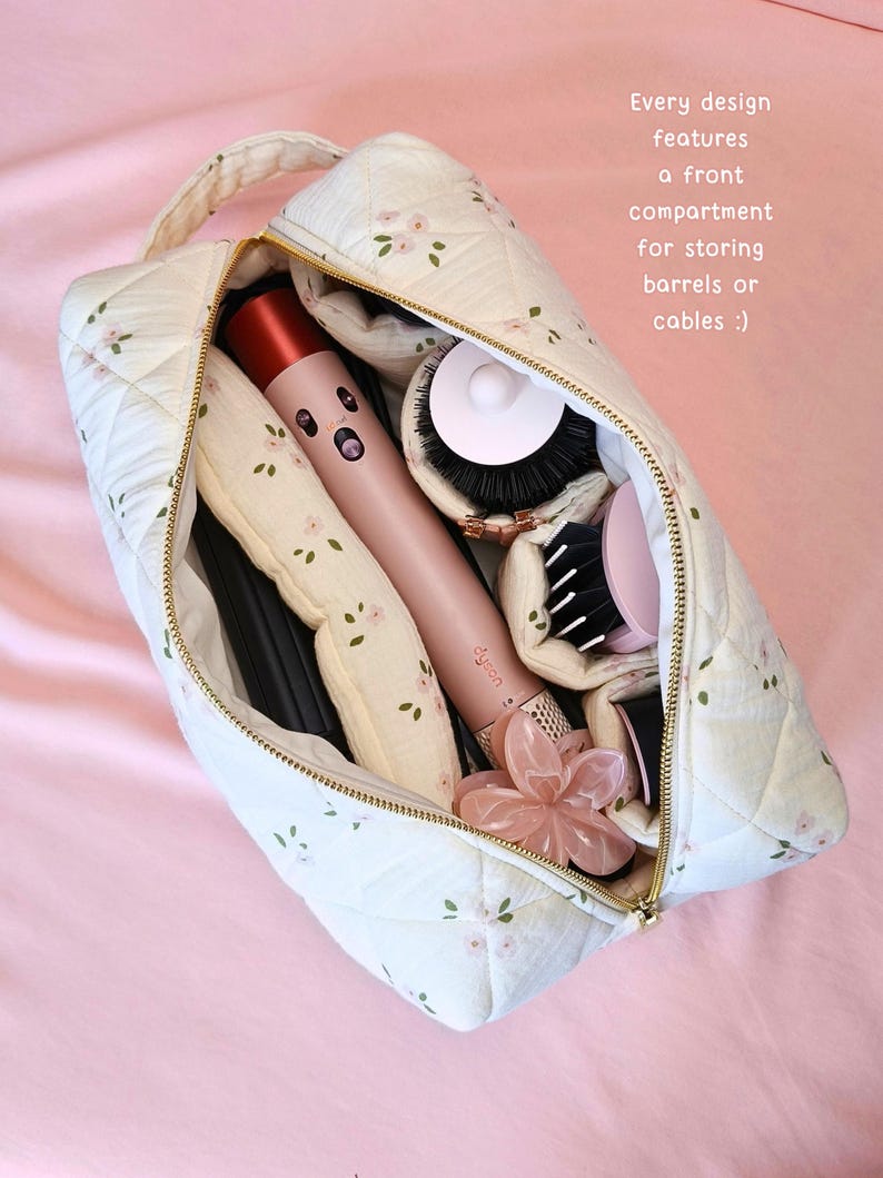 May include: A quilted cream-coloured storage bag with a delicate pink floral pattern, featuring a gold zip and a top handle. The bag contains a pink hair styling tool, various round brush attachments, and a flower-shaped hair clip. Text reads: Every design features a front compartment for storing barrels or cables :)