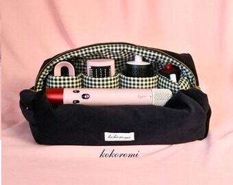 May include: A black fabric storage bag with a white and black gingham interior lining. The bag contains a pink Dyson hair styling tool and four cylindrical compartments holding various hair styling attachments. A white label reads kokoromi.