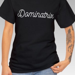 May include: A black t-shirt with the word "Dominatrix" written in white cursive script.