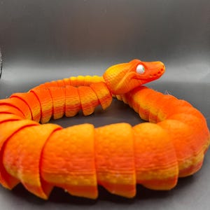 Peut inclure: Jouet serpent segment&eacute; orange et jaune avec un &oelig;il blanc. Le serpent est enroul&eacute; en cercle.