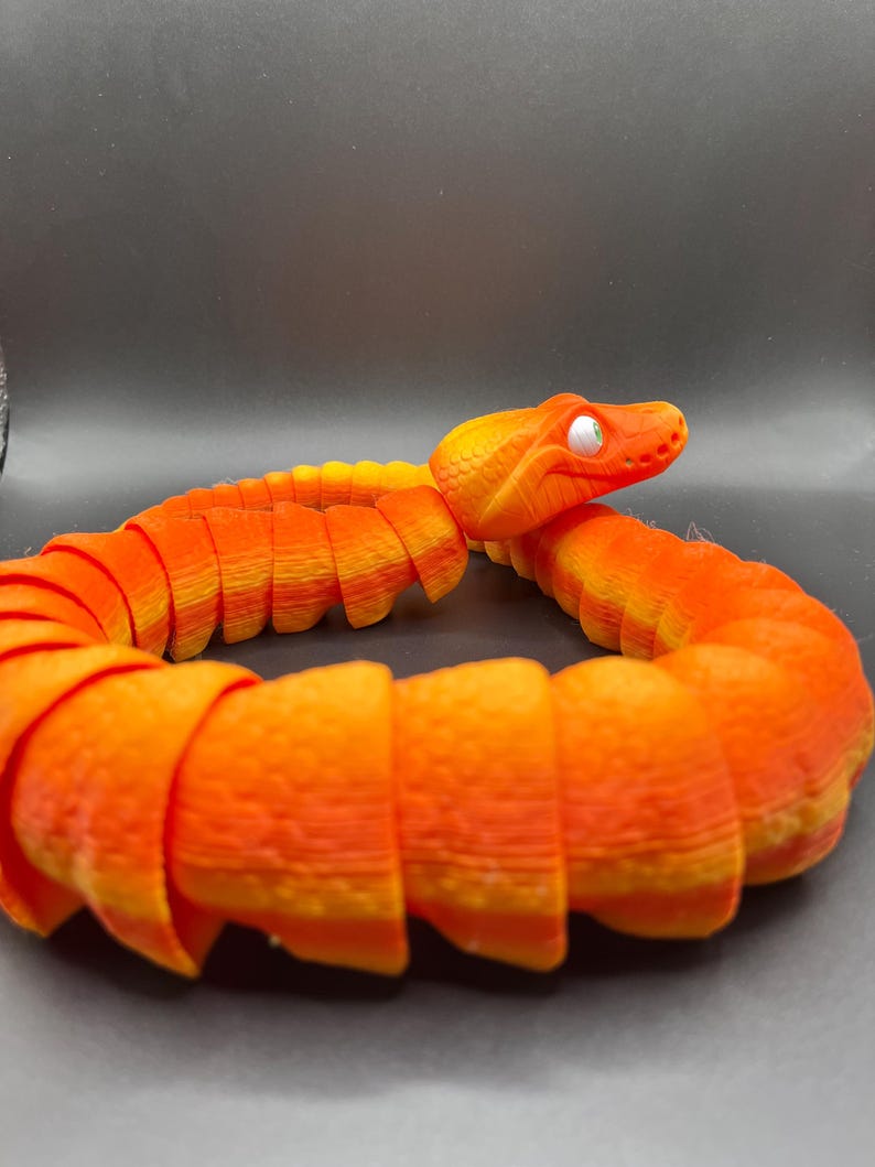 Peut inclure: Jouet serpent segment&eacute; orange et jaune avec un &oelig;il blanc. Le serpent est enroul&eacute; en cercle.