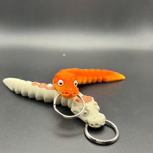 Può includere: Due portachiavi a forma di verme arancioni e bianchi con un anello portachiavi argentato. Il verme arancione ha un viso con occhi e una bocca. Il verme bianco ha un viso con occhi e una bocca.