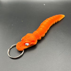 May include: Orange and yellow plastic keychain shaped like a worm with a silver key ring.