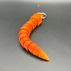 May include: Orange segmented worm keyring with a silver ring. The worm is curled into a C shape.