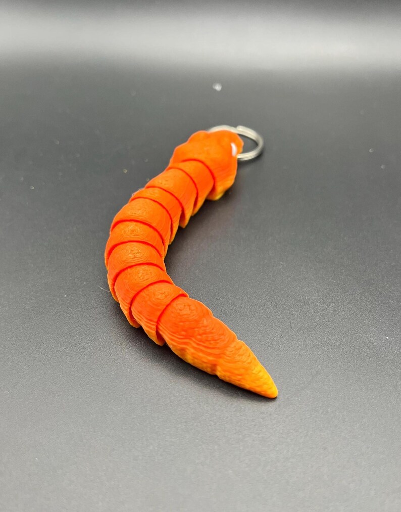 May include: Orange segmented worm keyring with a silver ring. The worm is curled into a C shape.