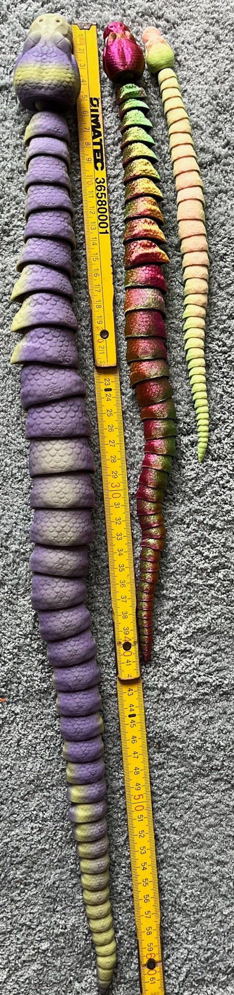 Peut inclure: Trois serpents en plastique articul&eacute;s. Le serpent violet est le plus long, suivi du serpent vert et rouge, puis du serpent jaune et rose. Les serpents mesurent environ 45 cm de long. Une r&egrave;gle jaune est &agrave; c&ocirc;t&eacute; des serpents.