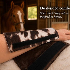 May include: A dual-sided wrist wrap featuring a brown and white cow-print pattern on one side and a solid dark brown texture on the other. The wrap includes black hook-and-loop fastener strips. Text reads: Dual-sided comfort. Slick side & cozy side—inspired by horses.