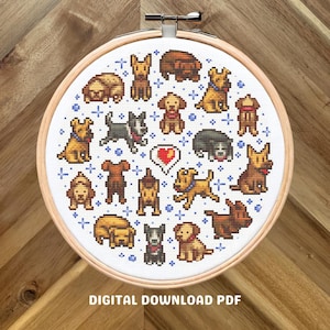 May include: A cross-stitch embroidery hoop with a design of various dog breeds in a pixelated style. The design includes a heart and blue star accents. The text "DIGITAL DOWNLOAD PDF" is at the bottom. The hoop is set against a wooden background.
