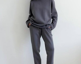May include: A gray hooded sweatshirt and matching sweatpants. The sweatshirt has a drawstring hood and a relaxed fit. The sweatpants have a drawstring waistband and a cuffed hem.