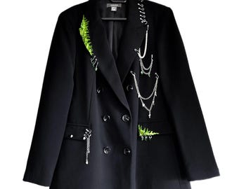 May include: A black double-breasted blazer with decorative silver chains and green embroidered accents. The blazer features a notched lapel, four buttons, and is hanging on a black hanger.