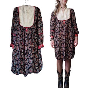 Puede incluir: Un vestido largo de manga larga con estampado de paisley, superposición de encaje blanco y ribete rojo. El vestido tiene un cuello alto y una falda fruncida.