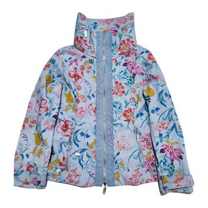 Op de afbeelding: Een lichtblauw jack met een bloemenprint. Het jack heeft een hoge kraag en een ritssluiting. De bloemenprint is in tinten roze, rood, geel en blauw.