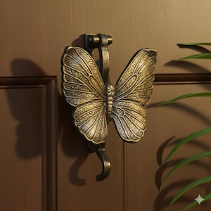 Puede incluir: Un llamador de puerta con forma de mariposa de color bronce. Las alas de la mariposa están detalladas con patrones de venas. El llamador está montado en una puerta marrón. El diseño añade un toque decorativo a cualquier entrada.