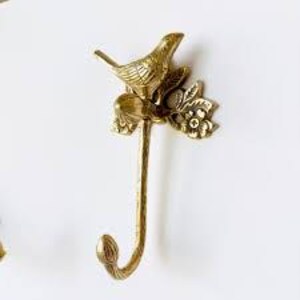 Puede incluir: Un gancho de pared de color lat&oacute;n con un p&aacute;jaro detallado posado en una rama floral. El gancho tiene un dise&ntilde;o curvo y es adecuado para colgar objetos. La pieza decorativa es de metal y tiene una est&eacute;tica vintage.