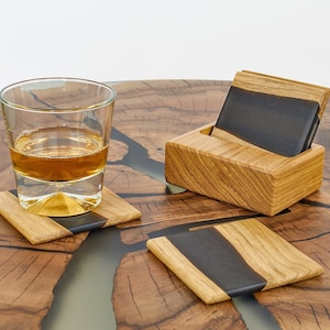 Może przedstawiać: Zestaw czterech drewnianych podkładek z wkładką z czarnej żywicy, szklanka whisky na jednej podkładce i drewniany stojak na podkładki.